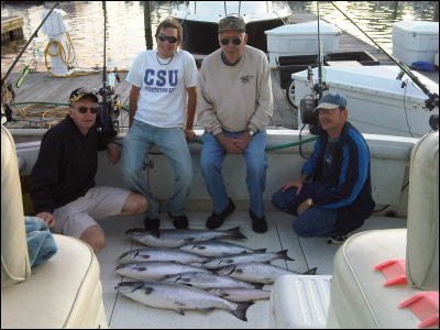 group of 4 on a boat in front of their fish that they caught