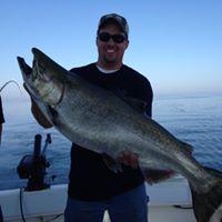 A man standing on a charter boat while carrying a huge Chinook Salmon caught with the help of Captain Jason from Reel Sensation