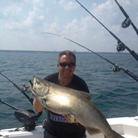 A man holding a large king salmon trophy fish while standing on Reel Sensation’s charter boat on Lake Michigan